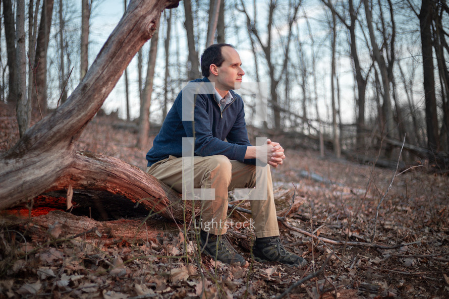 Man sitting on fallen tree in the woods gazing away