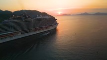 Panoramic vertical aerial view of a cruise ship traveling over the ocean during golden summer sunset time
