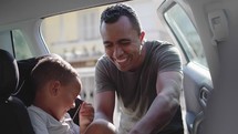 Loving father puts his little cute male child in back seat and makes him smile being playful
