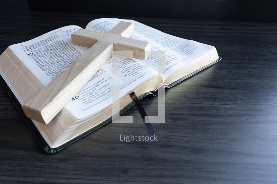 Cross laying on open bible on a dark wood table