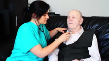 Nurse checking sick senior man with stethoscope at home