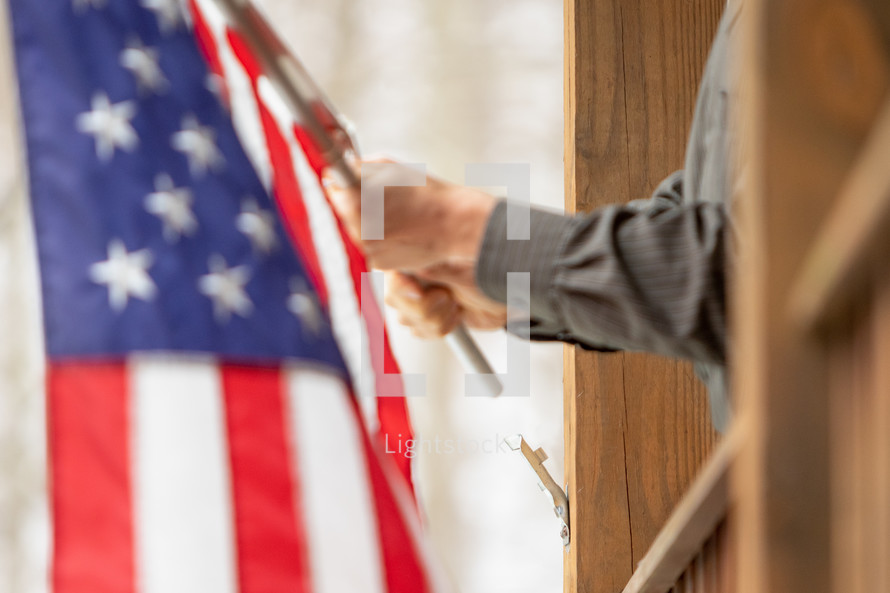 Man mounting American flag on wooden porch post