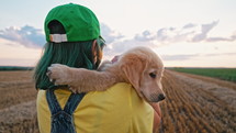 Sweet golden retriever puppy with its owner woman walking on hands. Happy dog spending good time on nature, field background. Cute doggy. Hunting breed.