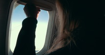 Woman opening and looking out an airplane window.