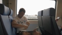 View of young man sitting in the train and using laptop 