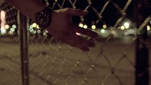 a man walking with his hand against a chain linked fence 