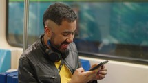 Young man holds smartphone and smiling while traveling by subway. Recording voice message.
