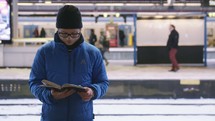 a man reading a Bible in a busy subway 
