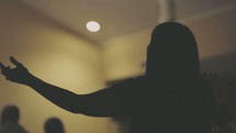 Silhouette of a woman with her arms outreached at a worship service.