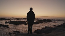 young man standing near the ocean deep in thought 