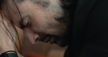 Young, emotional, anxious, and stressed man with long hair and black suit sitting in old church in worship and praying.