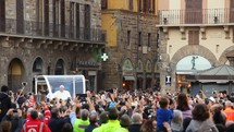Pope Francis driving through a city street with a large crowd of people waving at him.