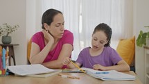 Mother helping her young daughter prepare homework during homeschooling