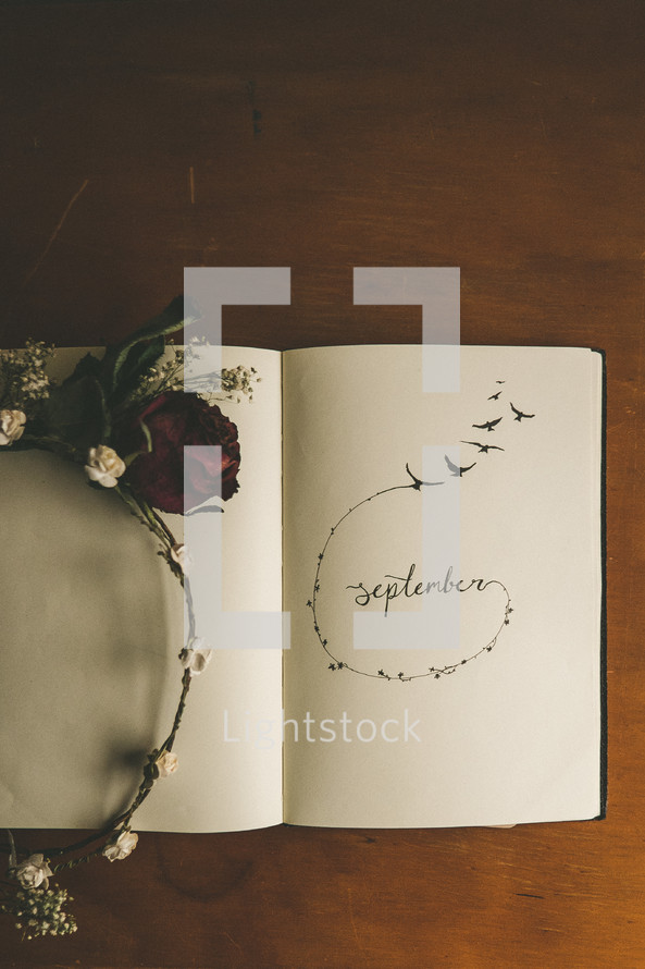 "September" written in an open book, with flowers upon it.