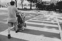 a father pushing his baby in a stroller across a crosswalk 