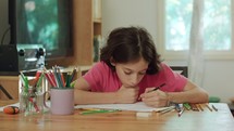 young girl sitting at the table drawing with colored pencils