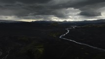 River flowing through dark landscape in Iceland, aerial view with mountains and scenic clouds in the background
