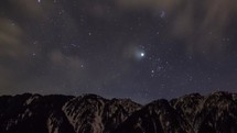 Timelapse of cloud movement and stars over a mountain range.