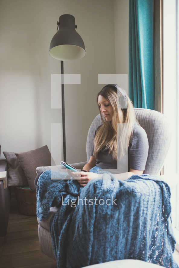 a woman sitting in a chair listening to a Bible app with headphones 