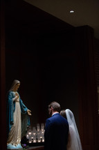 bride and groom praying before a statue of Mary 