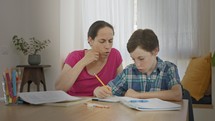 Mother helping her young son prepare homework during homeschooling