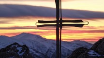 Catholic cross on top of a mountain in winter.Iron wrought iron cross commemorating the crucifixion of Jesus.In the background pastel colored clouds at the end of the day