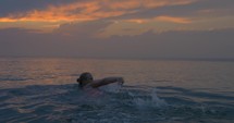 Young woman swims away in the sea at sunset