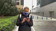 Woman wearing a medical face mask while walking and looking at her phone.