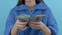 Woman counting cash money - USD currency 100 dollars banknotes on blue background. Jackpot, lottery prize, salary, profitable investment