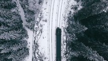 aerial view over train tracks covered with snow and a moving train 
