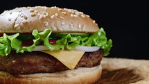 Big appetizing burger with meat, onion, vegetables, melted cheese, lettuce and mayonnaise sauce on parchment. 