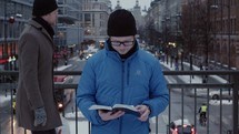 a man standing in a busy city reading a Bible amongst the distractions 