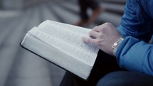 a man sitting on steps in a city reading a Bible 
