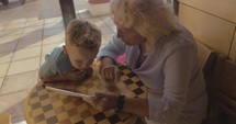 Boy and grandmother entertaining with touch pad in cafe