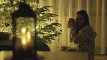 A Girl Seated Next to the Christmas Tree, Holding a Gift and Gently Touching the Hanging Decorations - Close Up