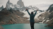 Female Hiker Raising Hands In The Air Facing Laguna de los Tres And Fitz Roy Mountain In Patagonia, Argentina.