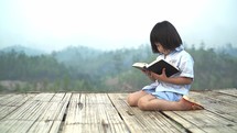 Little girl reading her Bible in a mountain landscape.