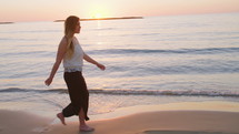 Tracking shot of a young woman walking on the beach during sunset