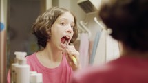 young girl brushing her teeth in front of the mirror