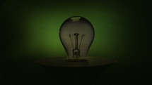 Real light bulb turning on, shine and flickering on green background.