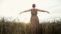 Elegant woman enjoying, rejoices, rising hands to sun in wheat field. Amazing nature landscape, feminine dress, young unrecognizable lady back portrait. High quality 4k footage