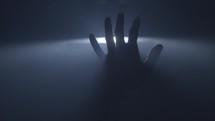 a reaching hand behind a spotlight 