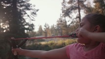 Young girl shooting a slingshot in the forest. - 1 of 2