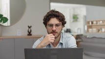 Thoughtful young businessman sitting at remote workplace with laptop computer. Pensive professional thinking at table in office. Focused business man face looking around. Serious man portrait
