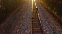 a man walking down railroad tracks under bright sunlight 