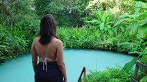 Young exotic woman entering in natural tropical pool. Tropical Paradise with vegetation in background, slow motion.
