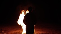 A young man watching a large fire with engulfing flames in cinematic slow motion.