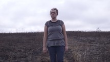 a woman walking through a burnt field 