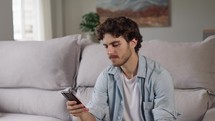 Closeup focused young man reading email on phone at home office. Portrait of male freelancer getting idea at remote workplace. Handsome guy texting on smartphone on couch
