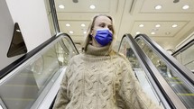 Woman wearing a mask riding an escalator at a shopping mall.